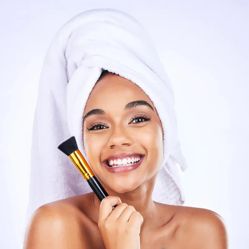 Jeune femme souriante, serviette sur la tête, un pinceau de maquillage à la main
